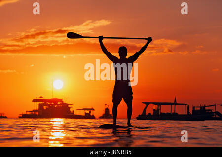 La palette active boarder. Coucher du soleil noir silhouette de jeune sportsman paddling on stand up paddleboard. Mode de vie sain. Sport d'eau, surf SUP Banque D'Images