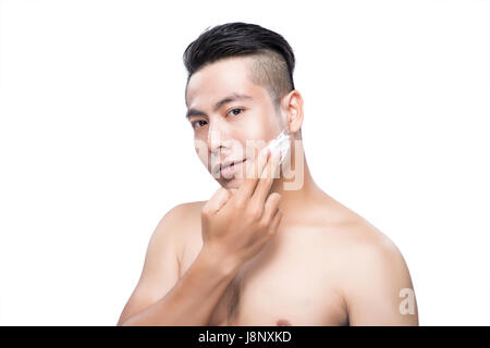 Young Asian man shaving sur fond blanc, looking at camera Banque D'Images