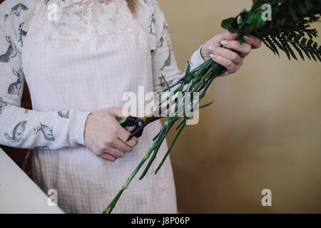 Fleuriste femme tablier de coupe des tiges de fleurs à l'intérieur. Female florist bouquet dans la préparation d'un fleuriste. close up Banque D'Images