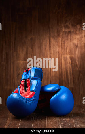 Paire de gants de boxe rouge et bleue sur la surface en bois contre fond de bois. Banque D'Images