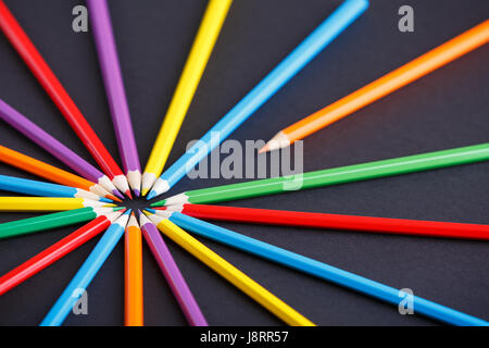 Un crayon orange se démarquer de le cercle d'autres crayons colorés sur le fond sombre Banque D'Images