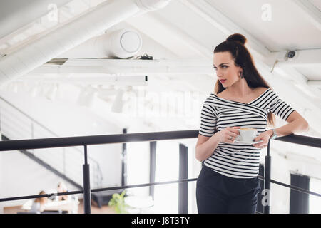 Portrait de femme debout et tenant une tasse de café et de cappuccino. Femme adulte heureux à l'écart de l'appareil photo. Banque D'Images