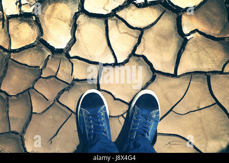 Pieds de ci-dessus, sur la terre sèche. Chaussures bleu gros plan sur l'arrière-plan du sol fissuré. Banque D'Images