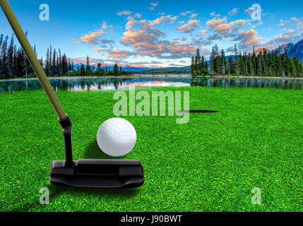 À l'aide d'un club de golf putter pour frapper une balle de golf sur un magnifique parcours de golf avec des lacs et des paysages de montagne tôt le matin. Banque D'Images