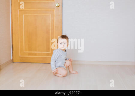 Mignon bébé garçon assis sur le sol dans la chambre Banque D'Images