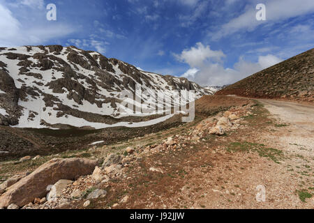 Paysage de montagne avec route sinueuse et les pics couverts par la neige fondante tourné aux beaux jours Banque D'Images