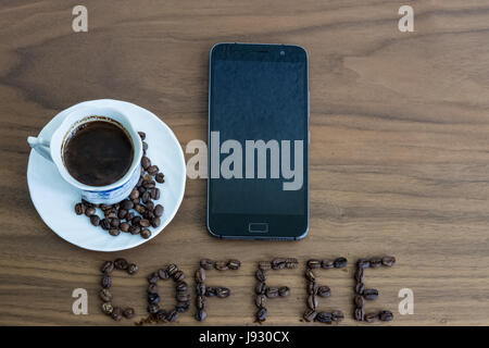 Les grains de café torréfié, éparpillés sur la table et à l'écrit, du café dans une tasse de café torréfié, plus de café, et d'un téléphone mobile, la texture du bois brun, l'arrière-plan Banque D'Images