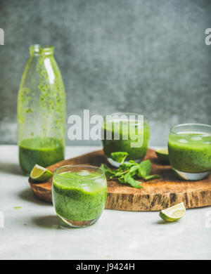 Smoothie frais en bouteille et des verres avec des cubes de glace, menthe, lime sur planche de bois, mur de béton gris à l'arrière-plan, selective focus, copiez l'espace. Nettoyer Banque D'Images