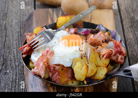 Petit-déjeuner de l'agriculteur avec pommes de terre rissolées, d'œufs et bacon frit servi dans une poêle de fer Banque D'Images