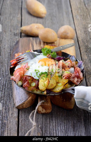 Petit-déjeuner de l'agriculteur avec pommes de terre rissolées, d'œufs et bacon frit servi dans une poêle de fer Banque D'Images