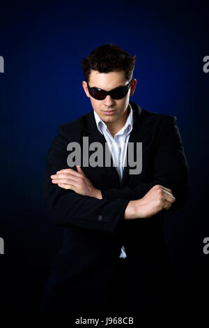 Jeune homme portant costume et lunettes de soleil sur fond sombre Banque D'Images