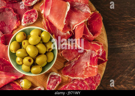 Une photo prise à la verticale d'une assiette de charcuterie espagnole avec jambon et saucisse cafe, aux olives vertes, sur un fond rustique foncé avec une place pour le texte Banque D'Images