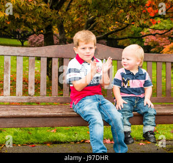 Deux jeune garçons assis sur un banc en bois, Roath Park, Cardiff, Pays de Galles, Royaume-Uni Banque D'Images