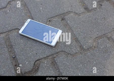 Téléphone avec écran brisé gisant sur le trottoir Banque D'Images