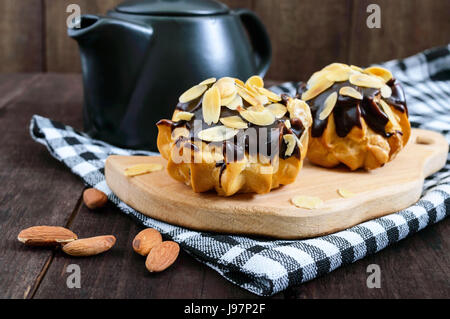 Éclairs, couverts de chocolat noir et flocons d'amandes de décoration en bois sombre sur un arrière-plan. Banque D'Images