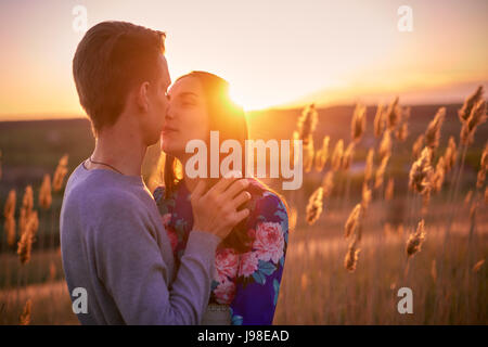 Garçon et une fille au coucher du soleil s'embrasser dans le domaine un soir d'été Banque D'Images