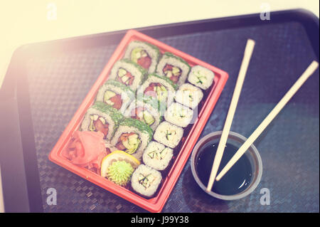 Les sushis japonais en rouge en plastique pour transporter la nourriture sur noir. Faites des rouleaux de viande de crabe, avocat, concombre à l'intérieur et de l'éperlan masago re à l'extérieur. Banque D'Images