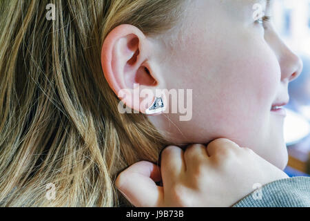 Vue rapprochée d'une jeune fille de 11 ans de son contour d'oreille en émail ou de son goujon sous la forme de Une chaussure d'entraînement de type Converse Banque D'Images