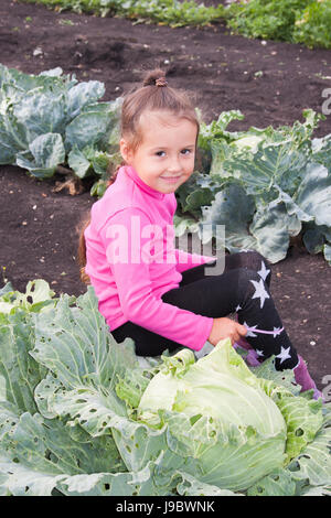 Petite fille est assise dans le chou dans le jardin un jour d'été Banque D'Images