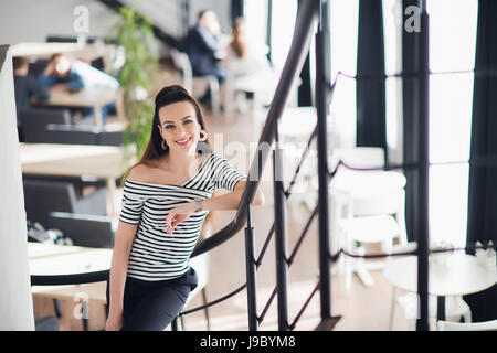 Portrait d'élégante femme d'âge moyen debout dans un café après le travail ou pendant les pauses tout en regardant la caméra et sourit. Banque D'Images