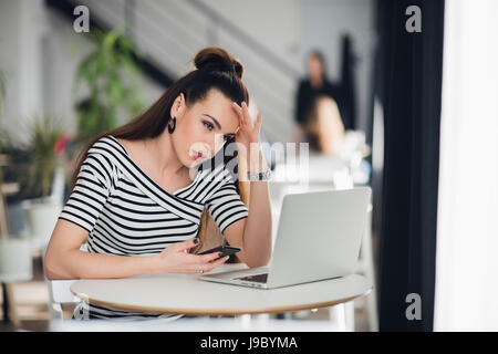 Femme journaliste talentueux pensif attrayant est la réflexion sur des solutions créatives pour faire de l'article travailler dans un café, charmant designer qualifiés de noter des idées pour démarrer en son smartphone. Banque D'Images