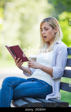 Jeune femme est assis dans un parc et la lecture de livre. Banque D'Images