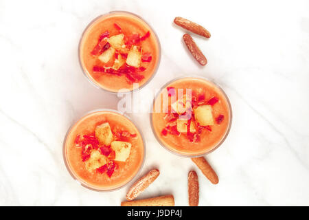 Une photo prise à la verticale d'un salmorejo, soupe froide espagnole traditionnelle, servie dans des verres avec des bâtonnets de pain, garnie de jambon et croûtons Banque D'Images