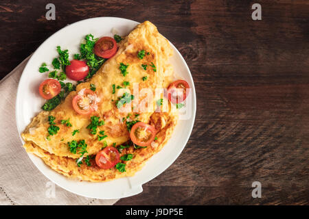 Une photo d'une omelette aux tomates cerises, le persil et le fromage râpé, tourné à partir de ci-dessus sur une texture rustique en bois avec une place pour le texte Banque D'Images