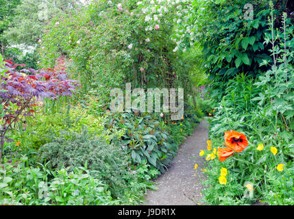 Chalet jardin d'été colorés avec une pierre chemin à travers les roses, fleurs, arbustes et arbres . Banque D'Images