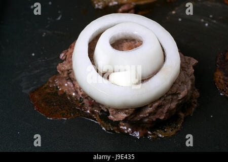 Matières de cuisson burger de cerf garnie d'oignons, dans poêle anti-adhésive sur le dessus d'une cuisinière électrique, gros plan Banque D'Images