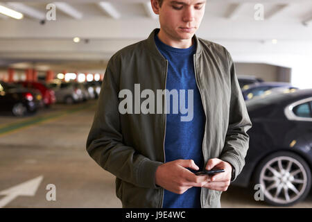 L'envoi de l'homme Text Message On Mobile Phone In Car Park Banque D'Images