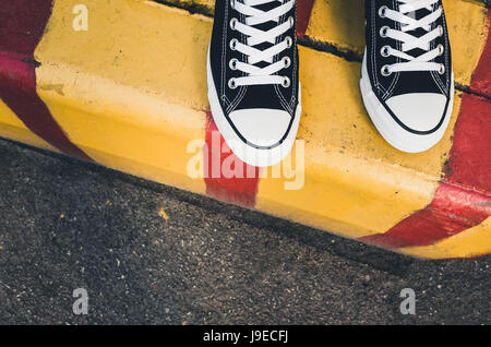 Le noir et blanc nouvelles sneakers, adolescent pieds debout sur jaune rouge urbains, routiers et frontière. Photo Gros Plan avec selective focus Banque D'Images