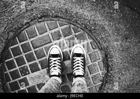 Adolescent pieds de sneakers. Un permanent Gumshoes couvercle de trou d'urbains. Libre photo en noir et blanc avec focus sélectif, old style Banque D'Images
