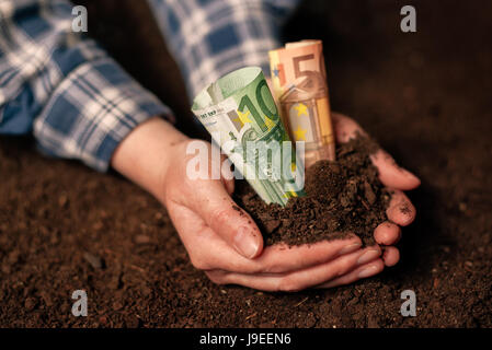 Les mains avec un sol fertile et de l'argent euro banknotes, female farmer poignée de terres cultivées qui fait de profit et de revenu régulier de l'aménagement durable d'agricu Banque D'Images