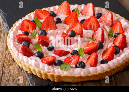 Tarte aux fraises avec crème chantilly rose, menthe et bleuets close-up sur la table horizontale. Banque D'Images