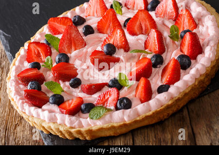 Tarte aux fraises fraîches avec de la crème fouettée, de menthe et de bleuets close-up sur la table horizontale. Banque D'Images