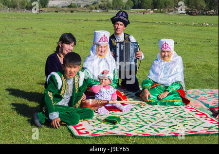 La famille kazakhe en vêtements traditionnels à écouter la musique d'un joueur d'accordéon, pour un usage éditorial uniquement, le sati village, Tian Shan, de Kazakhs Banque D'Images