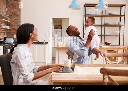 La mère travaille à la maison comme le père détient sa petite fille Banque D'Images