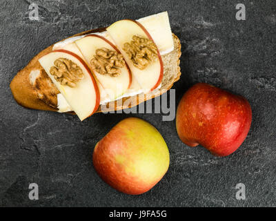 Les tranches de pommes avec brie Fromage et noix sur baguette grillées contre un arrière-plan en ardoise noire Banque D'Images