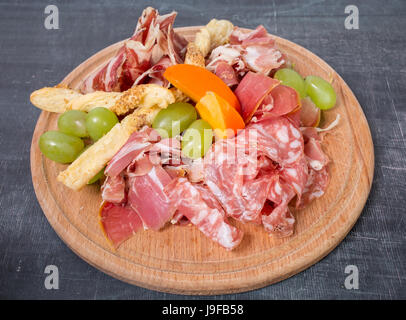 Assiette de viande séchée italienne mixte avec des croûtons et des raisins. Plaque située sur un tableau noir en arrière-plan. Banque D'Images