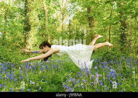 Jeune femme entre en lévitation bluebell flowers in British woodland Banque D'Images