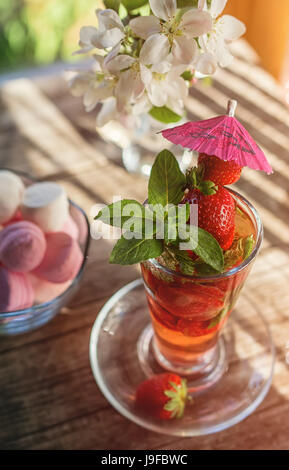 Boisson Detox de fraises et de menthe dans une tasse en verre sur l'arrière-plan de la guimauves et bouquet de fleurs sur une table de bois sur une journée ensoleillée. Sel Banque D'Images