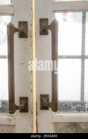 De longues poignées en métal sur les vieilles portes en bois avec peinture blanche ébréchée et sale des panneaux de verre Banque D'Images