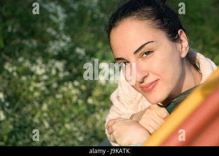 Portrait of a young woman looking at camera, assis sur une diapositive, l'extérieur du parc, confiant. Banque D'Images