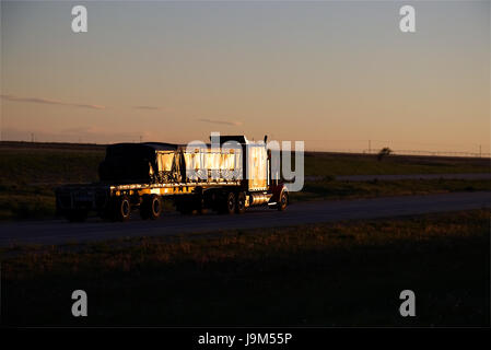 Un classique Semi-Truck tire une remorque à plateau chargé le long d'une autoroute nous rural au cours de la fin de l'après-midi heures. Banque D'Images