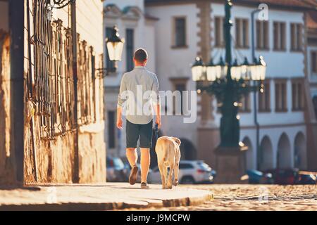 Matin dans la ville. Jeune homme marchant avec son chien sur la vieille rue au lever du soleil d'or. Prague, République Tchèque
