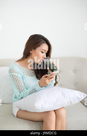 Asian woman sitting on couch using smartphone Banque D'Images