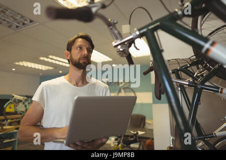 Employé réfléchie holding laptop tout en se tenant à l'atelier de vélo Banque D'Images