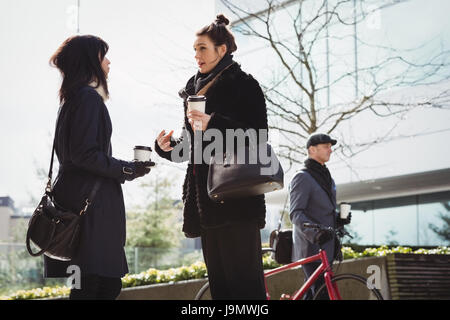 Businessman walking avec son cycle alors que les femmes en interaction les uns avec les autres dans les locaux à bureaux Banque D'Images