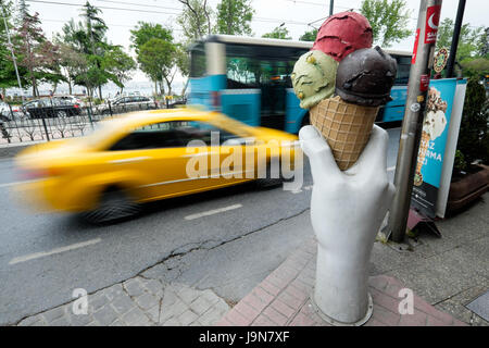 Une gigantesque main tenant une glace sur un trottoir à Istanbul, Turquie, avec un taxi jaune et de conduite d'autobus passé. Banque D'Images